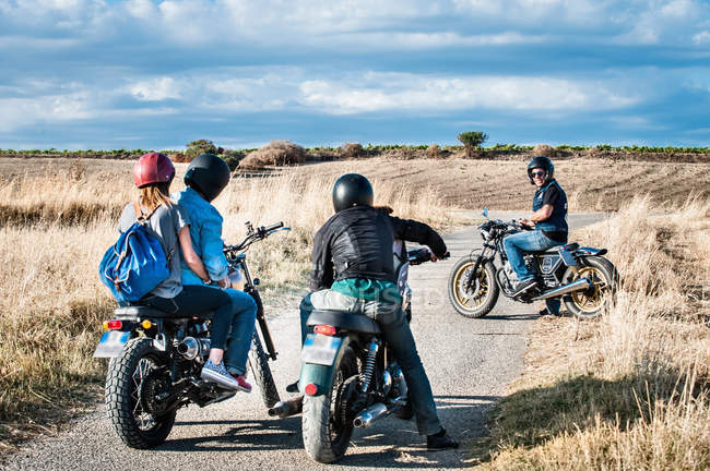 Vista trasera de cuatro amigos charlando en motocicletas en carretera rural, Cagliari, Cerdeña, Italia - foto de stock