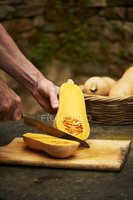 Männerhände hacken Butternusskürbis mit Messer auf Schneidebrett — Stockfoto