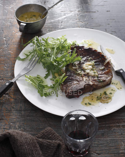 T-bone steak avec feuilles de salade mélangées sur assiette — Photo de stock
