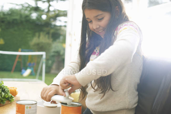 Menina na cozinha mesa de abertura lata de sopa de tomate — Fotografia de Stock
