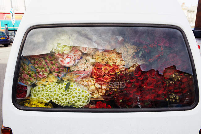 Hermosas flores varias en el maletero del coche, vista a través del cristal de la ventana - foto de stock
