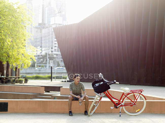 Young man taking break beside bicycle, Southbank, Melbourne, Australia — Stock Photo