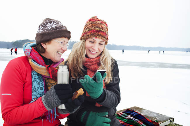 Las mujeres que beben caliente y mirando el teléfono inteligente - foto de stock