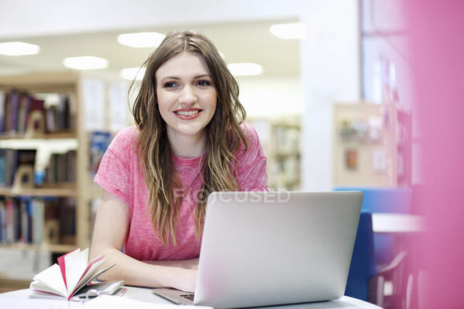 Jovem mulher usando laptop no interior da biblioteca — Fotografia de Stock