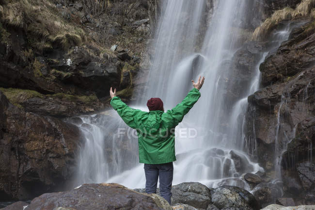 Man by waterfall arms out, Toce River, Premoselló, Verbania, Piedmonte, Italia - foto de stock