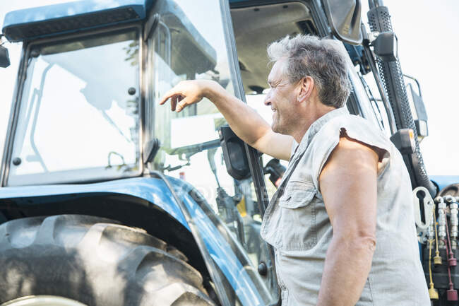Mature ouvrier agricole masculin appuyé contre tracteur — Photo de stock