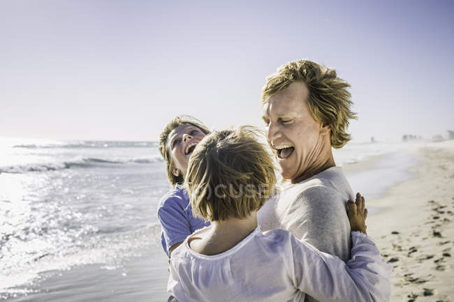 Padre che porta i figli in braccio sulla spiaggia — Foto stock