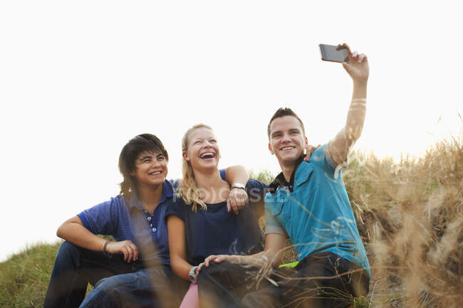 Teenagers sitting on sand dune taking self portrait photograph — Stock Photo