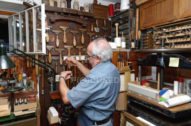 Uomo anziano che seleziona gli strumenti nel tradizionale laboratorio di rilegatura — Foto stock