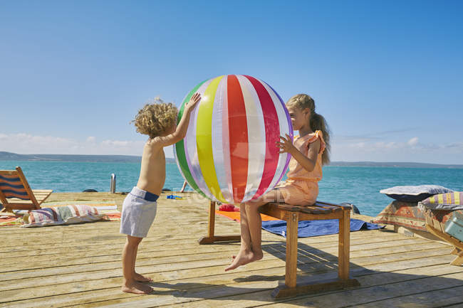 Мальчик и девочка играют с пляжным мячом на плавучей солнечной палубе, Краальбай, Южная Африка — стоковое фото