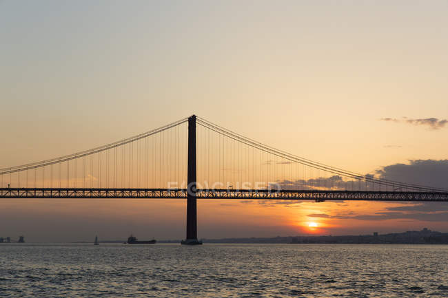 25 de Abril Bridge silhouette on sunset lighted sky — Stock Photo