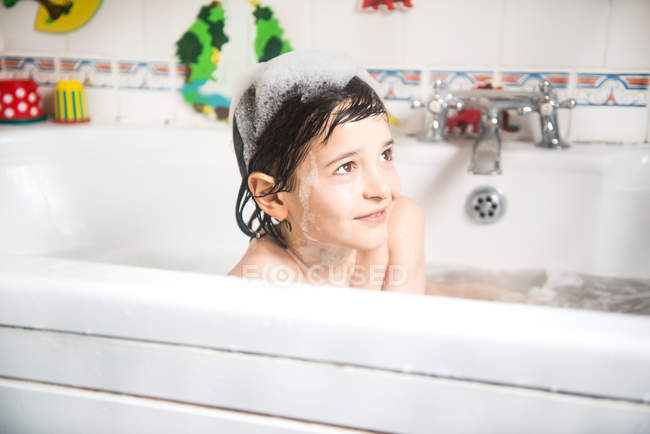 Мальчик сидит в ванной, пузырьки на голове, улыбается — стоковое фото