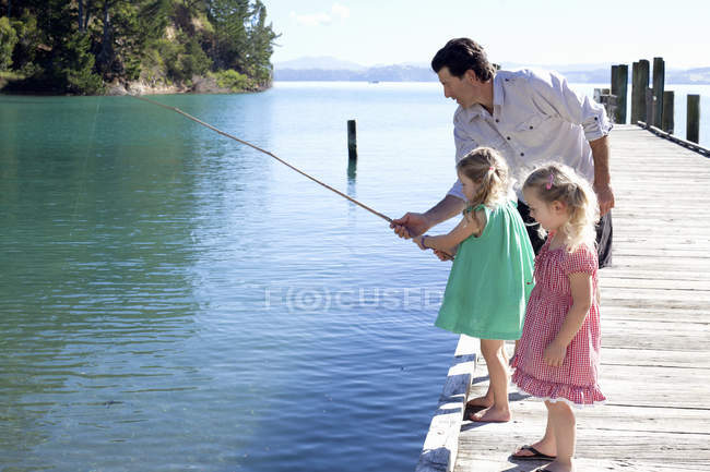 Зрілий чоловік і дві маленькі дівчинки рибалять з пірсу (Нова Зеландія). — стокове фото