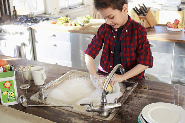 Маленький мальчик моет посуду на кухне — стоковое фото