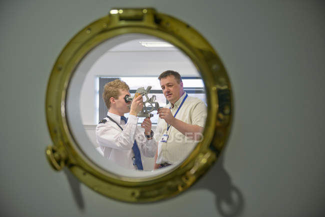 Tuteur enseignant aux élèves-officiers comment utiliser du sextant, voir à travers le hublot du navire — Photo de stock