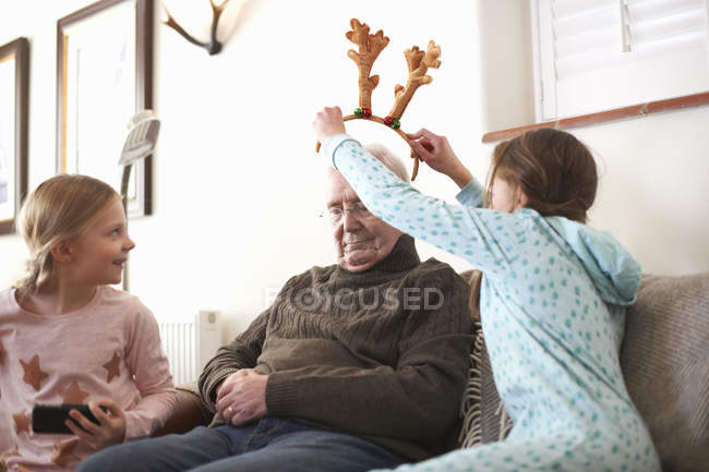 Sisters putting reindeer antlers on sleeping grandfather — Stock Photo