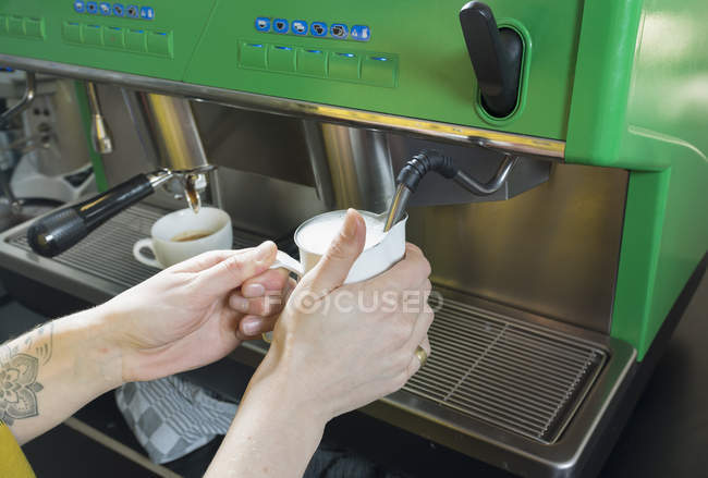 Mano de camarera tatuada preparando capuchino en cafetera - foto de stock