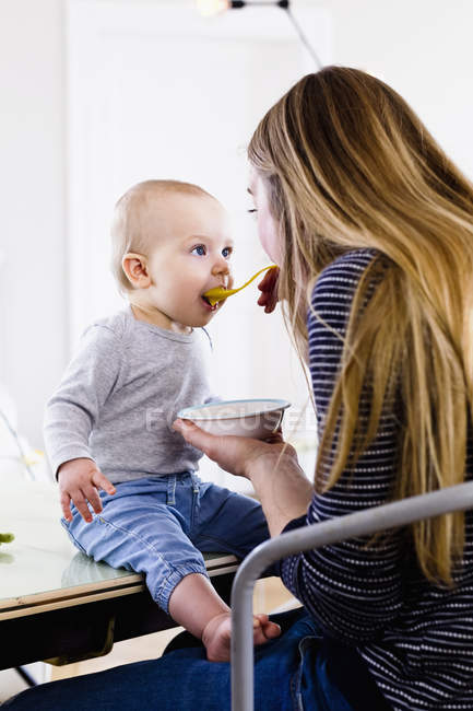 Femme adulte moyenne nourrissant bébé fille sur la table de cuisine — Photo de stock