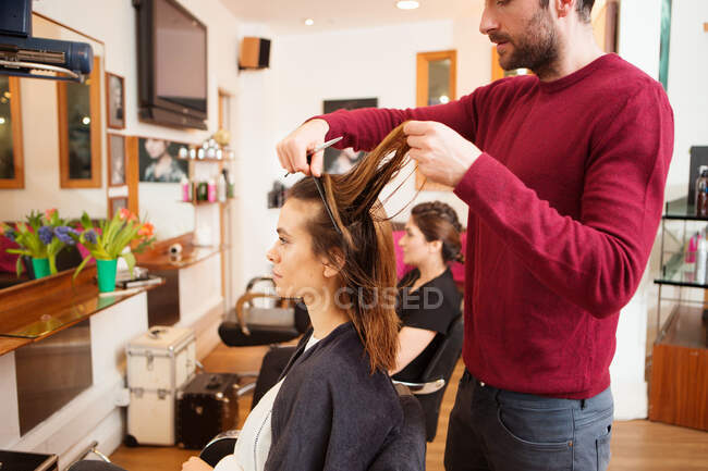 Cliente femenino que tiene el pelo largo y castaño recortado en peluquería - foto de stock