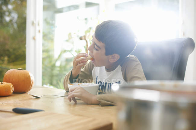 Menino comendo sopa de abóbora na cozinha — Fotografia de Stock