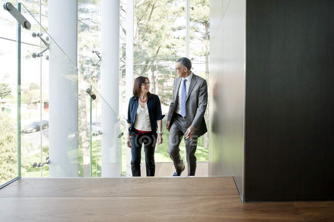 Businessman and woman walking up stairs in modern building — Stock Photo