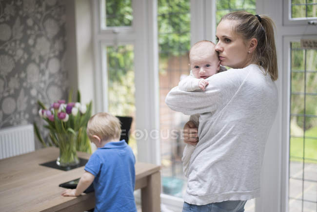 Mother holding baby boy, older son standing by table — Stock Photo