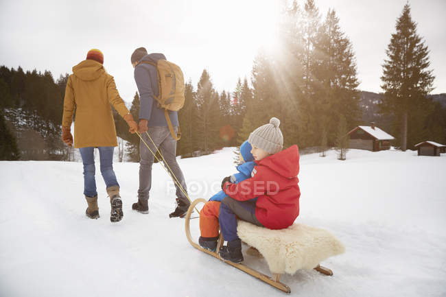 Visão traseira dos pais puxando filhos em tobogã na paisagem da neve, Elmau, Baviera, Alemanha — Fotografia de Stock