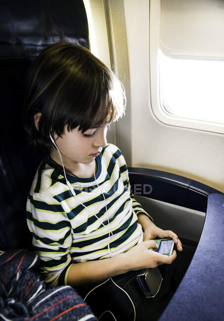 Мальчик на самолете выбирает музыку на mp3 плеере — стоковое фото
