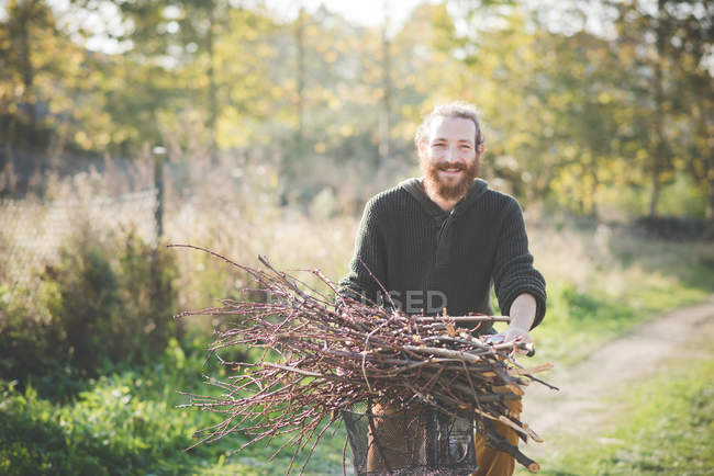 Young man carrying bunch of sticks on bicycle — Stock Photo