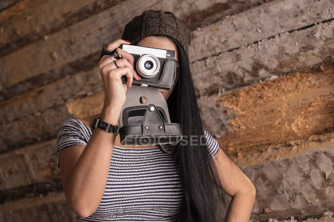 Портрет молодой женщины-фотографа, фотографирующей перед деревянной стеной — стоковое фото