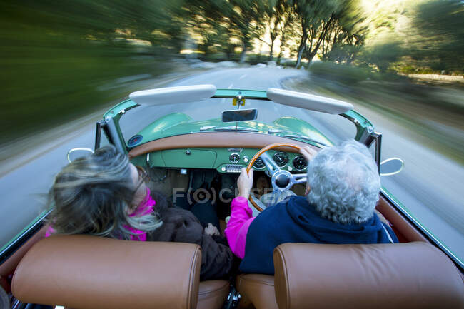 Visão traseira do casal sênior excesso de velocidade na estrada rural condução vintage conversível, Maiorca, Espanha — Fotografia de Stock