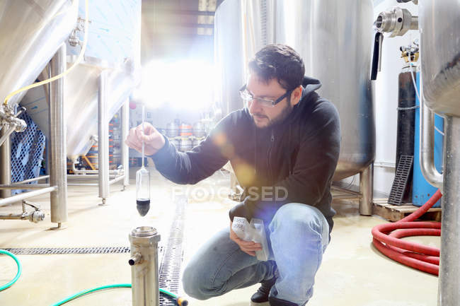 Worker in brewery, checking alcohol and sugar content of product — Stock Photo