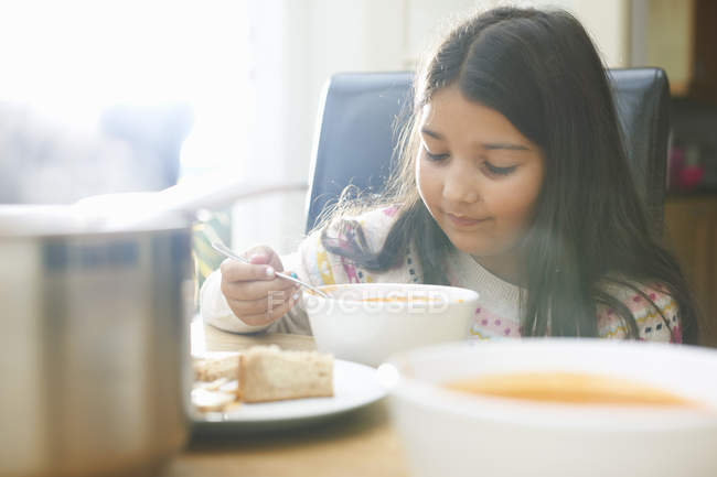 Girl eating bowl of soup in kitchen — Stock Photo