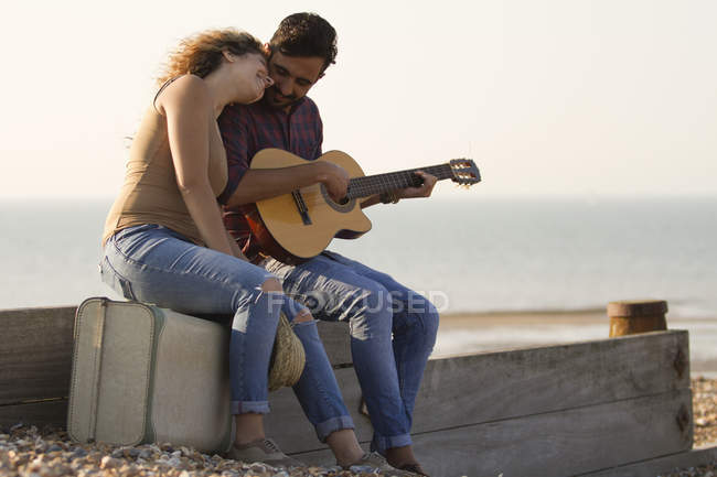 Pareja joven en la playa, hombre tocando la guitarra - foto de stock