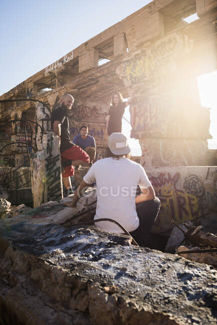 Hombres y mujeres jóvenes charlando en ruinas de minas iluminadas por el sol - foto de stock