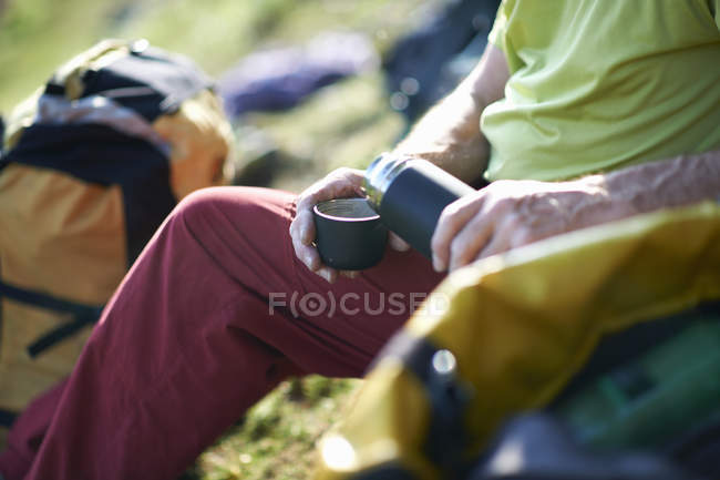 Vista recortada del excursionista vertiendo té del frasco - foto de stock