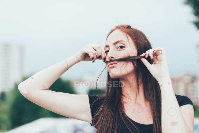 Портрет молодої жінки з веснянками, що роблять вуса довгим рудим волоссям — стокове фото