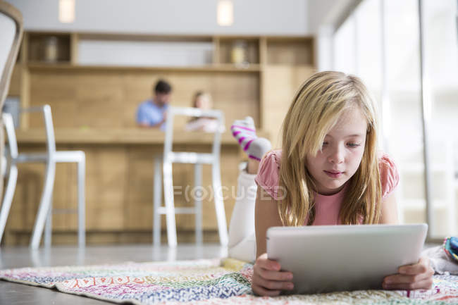 Mädchen liegt auf Teppich und surft mit digitalem Tablet im Wohnzimmer — Stockfoto
