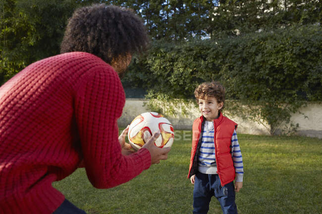 Батько і син грають з футболом в саду посміхаючись — стокове фото