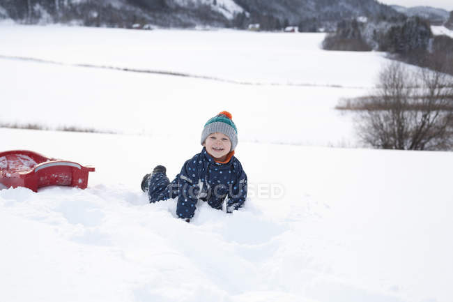 Menino brincando em seu tobogã na neve — Fotografia de Stock
