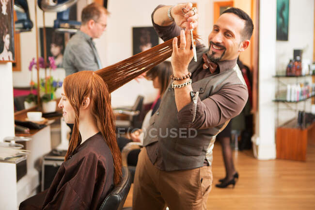 Cliente femenino que tiene el pelo rojo largo recortado en peluquería - foto de stock
