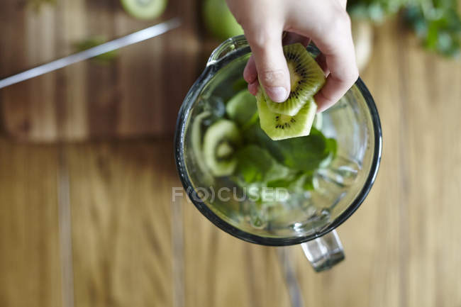 Cropped image of woman holding sliced green kiwi over blender — Stock Photo