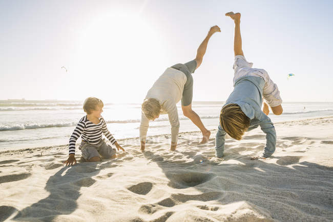 Padre e hijos en la playa haciendo puestos de manos - foto de stock