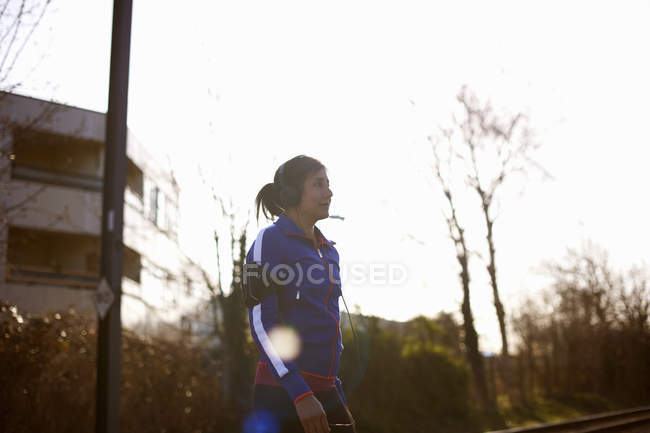 Mature female runner in park listening to music on headphones — Stock Photo