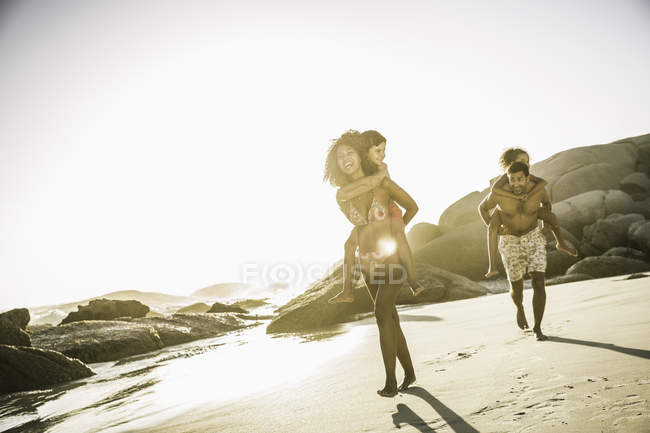 Родители катают детей на спине по пляжу — стоковое фото