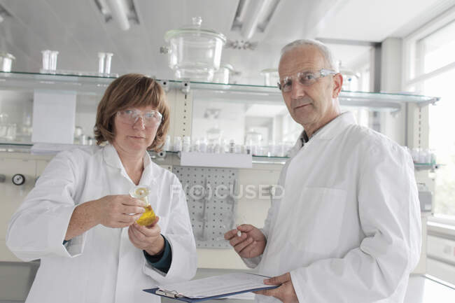 Científicos trabajando en laboratorio, sosteniendo líquido amarillo en el vial - foto de stock