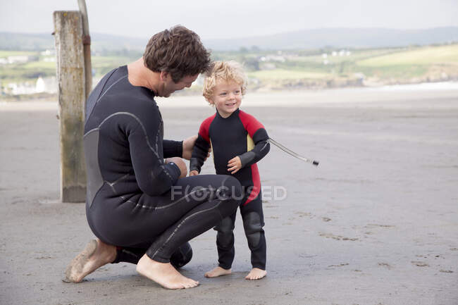 Father and son on beach wearing wet suits — Stock Photo