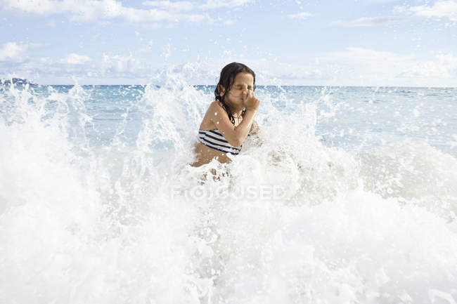 Fille jouer dans l'eau de mer tenant nez tout en jouant sur la plage — Photo de stock