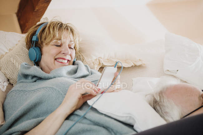 Mulher madura deitada na cama usando mp3 player — Fotografia de Stock
