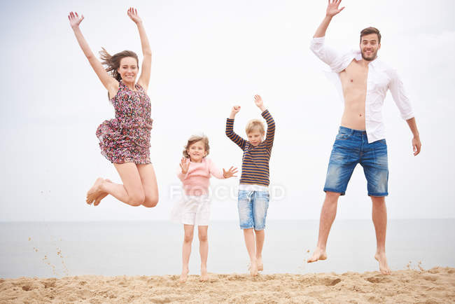 Família pulando na praia contra o céu juntos — Fotografia de Stock